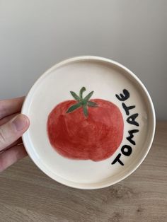 a hand holding a ceramic bowl with a tomato painted on the side that says, to make tomato