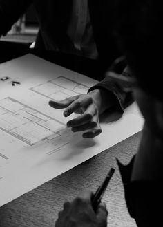 two people sitting at a table with papers and pens in their hands, one person is pointing to the floor plan