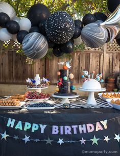 an outdoor birthday party with black and white balloons, cake and desserts on a table