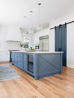 a large kitchen with blue cabinets and white counter tops on hard wood flooring that has an area rug in front of it