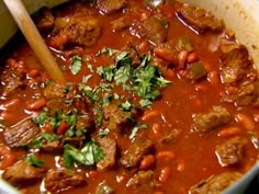 a pot filled with meat and vegetables next to a wooden spoon