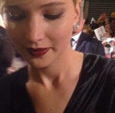 a close up of a person wearing red lipstick and black dress with people in the background