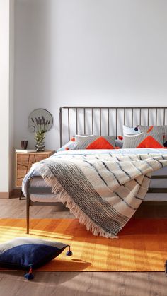 a bed sitting on top of a wooden floor next to a white wall with orange pillows