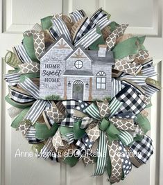 a wreath with a house on it and green ribbons hanging from the front door,