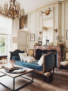 a living room filled with furniture and a chandelier hanging from the ceiling next to a fire place