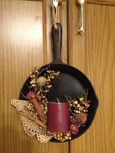 a frying pan with a candle, pine cones and other items hanging from it