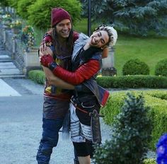 a man and woman hugging each other in front of some bushes on the side walk