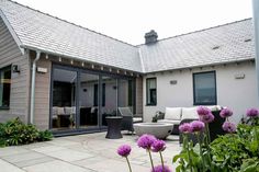 a patio with purple flowers in the foreground and an outdoor living area on the far side