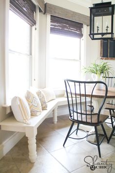 a dining room table with chairs and a bench in front of two windows that have roman shades on them