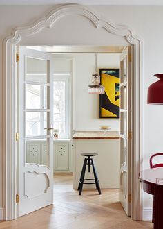 an open door leading to a kitchen with stools and a painting on the wall