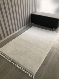 a white rug with tassels on the floor in front of a striped wall