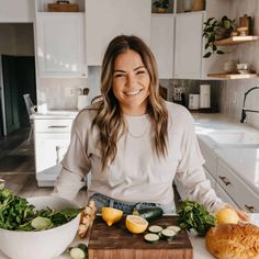 a woman standing in front of a cutting board with vegetables and bread on the counter