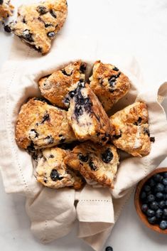 blueberry muffins in a bowl on top of a napkin next to some berries