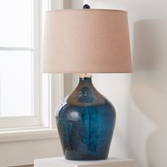 a blue vase sitting on top of a white table next to a lamp with a beige shade