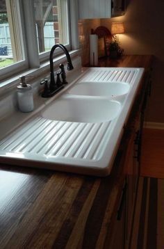 a kitchen sink sitting under a window in front of a counter top with two faucets