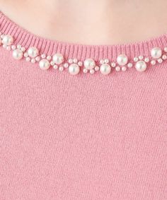 a woman wearing a pink sweater with pearls on it