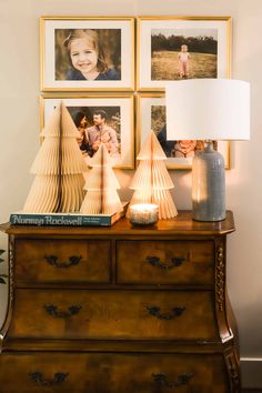 a wooden dresser topped with pictures next to a lamp