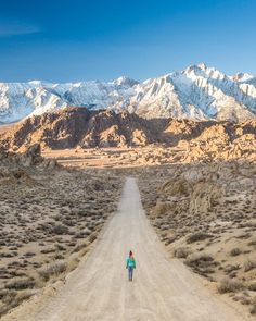 a person walking down a dirt road in the middle of nowhere with mountains in the background