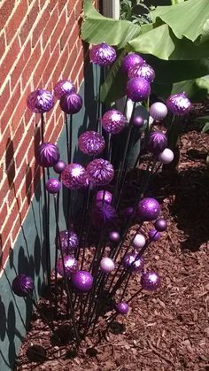 some purple balls are in front of a brick wall and plants with green leaves on the ground