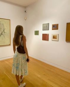 a woman standing in front of paintings on the wall and looking at them with her back to the camera