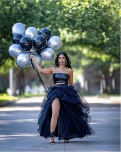 a woman in a black dress holding silver and black balloons while walking down the street