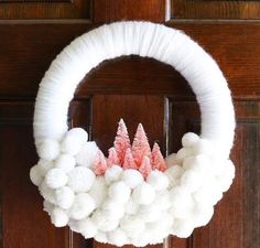 a white wreath decorated with pink and white pom - poms