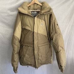 Men's Down-Filled 686 Ace Snowboarding Jacket. Made With A Nylon Outer Shell Material And Featuring A Full Zip Closure With Hook & Loop, And Snaps. The Jacket Is Mid-Length And Colored In A Khaki/Tan/Beige Monochrome Color Way, With Removable Faux Fur Trim Accents And A Geometric Pattern On The Back. It Has Many Great Pockets And Ways To Access The Interior, Side Vents, And A Safety Mirror (Plastic) In The Right Cuff. The Jacket Is Pre-Owned And Has Been Well-Maintained, With Just A Few Sirens D Tactical Winter Hiking Parka, Khaki Tactical Winter Outerwear, Techwear Parka For Winter Sports, Functional Beige Windbreaker For Winter, Insulated Long Sleeve Outerwear For Snowboarding, Insulated Long-sleeve Outerwear For Snowboarding, Insulated Outerwear For Snowboarding In Winter, Techwear Outerwear For Snowboarding Ski Season, Monochrome Color