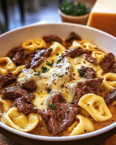 a white bowl filled with pasta and meat covered in sauce on top of a wooden table