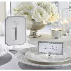 a table setting with white flowers and place cards on the plates, candles and napkins