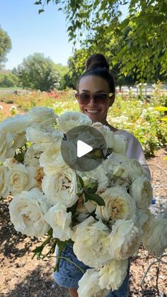 a woman holding a large bouquet of white flowers in her hands and smiling at the camera