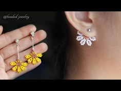 the woman is holding two pairs of yellow and white beaded earrings in her hand