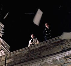 two people standing on top of a building with papers flying in the air above them