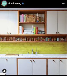 a kitchen with white cabinets and yellow tile backsplash, wooden shelves above the sink