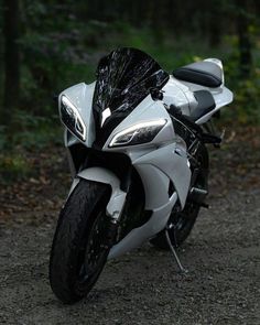 a white motorcycle parked on top of a dirt road next to trees in the woods