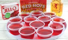 jello shots are arranged on a tray with red hots in the middle and two boxes of jello behind them