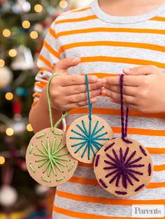 a person holding three ornaments in front of a christmas tree