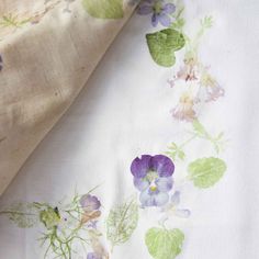 the fabric is white and has purple flowers on it, along with green leafy leaves