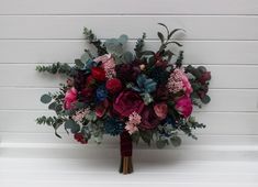 a bridal bouquet with red, purple and green flowers on a white wall background