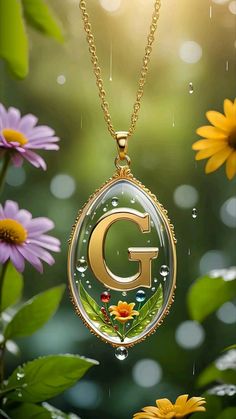 a necklace with the letter g on it and flowers in front of it, surrounded by raindrops