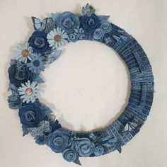 a blue wreath made out of jeans with flowers and butterflies on the front, sitting against a white wall