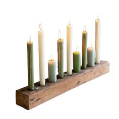 seven candles are lined up in a row on a wooden stand with one candle lit