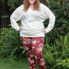 a woman standing in the grass with her hands on her hips wearing red floral pants