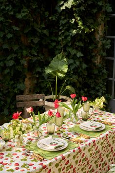 the table is set with plates, cups and vases on it in front of an ivy covered wall