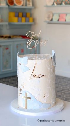 a white cake with gold lettering and a cross on top is sitting on a table