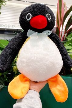 a hand holding a black and white stuffed penguin in front of a potted plant