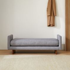 a gray couch sitting next to a coat rack on top of a wooden floor in front of a white wall