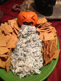 a green plate topped with chips and dip next to a jack - o'- lantern