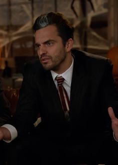 a man wearing a suit and tie sitting in a chair with his hands out to the side