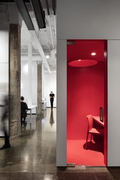 an open red door in the middle of a room with two people walking by it