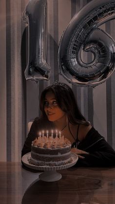 a woman sitting in front of a birthday cake with candles on it and the number six behind her